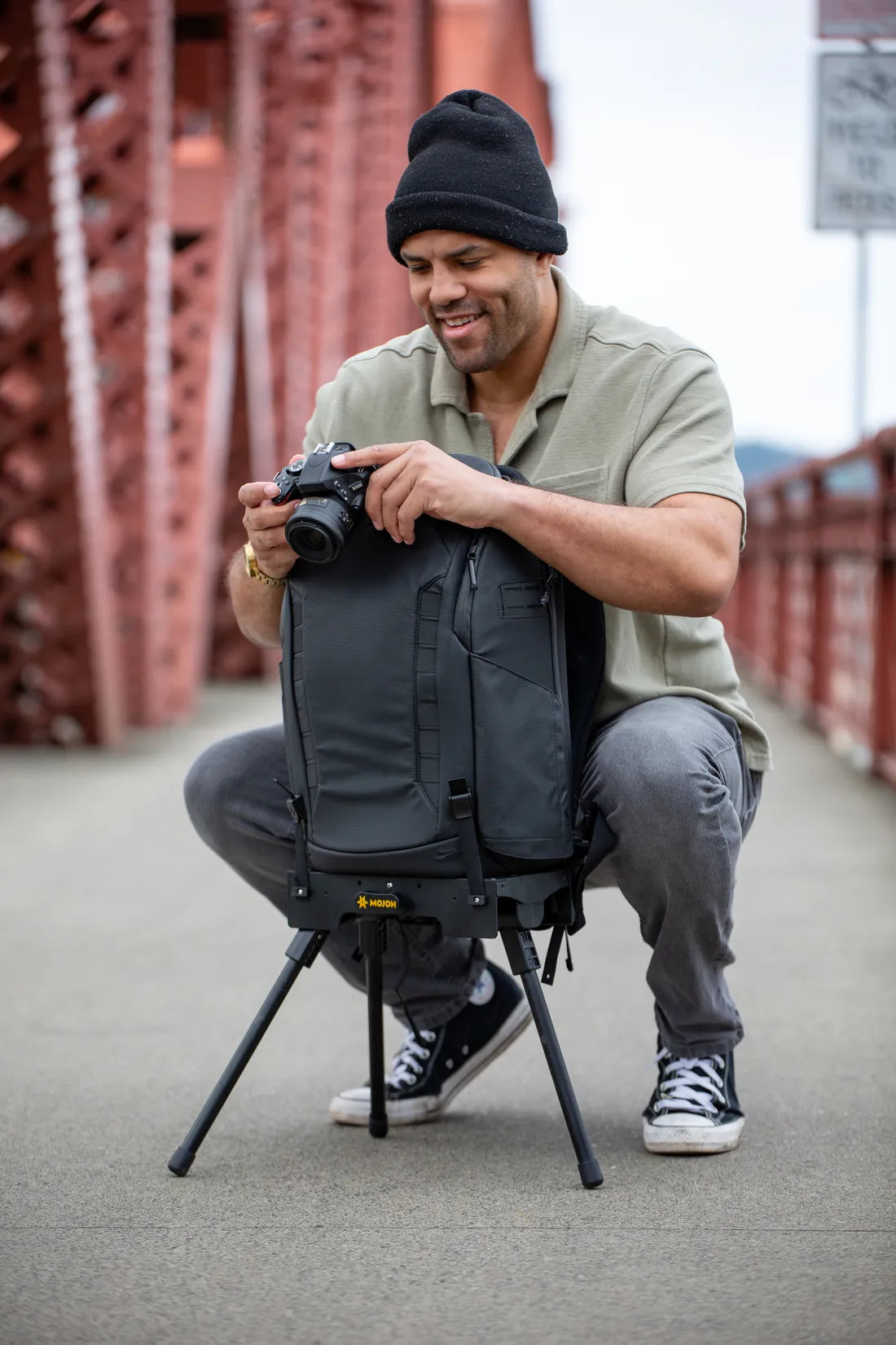 A photographer on a bridge swapping gear from a camera backpack held upright on the Ryzer Go