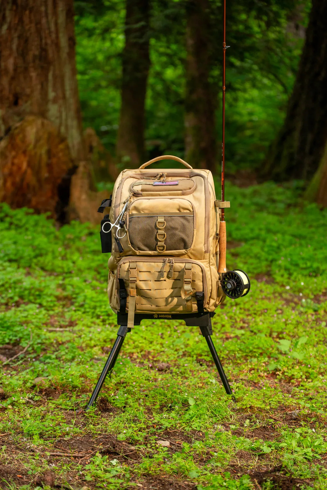 A fly fishing pack with a rod and reel held upright on the Ryzer Go in a forest clearing