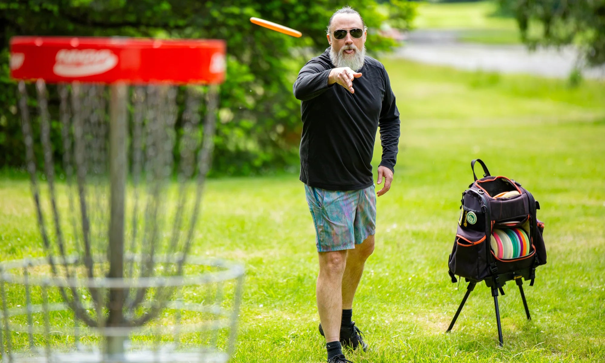 A disc golfer walking the course with the bag standing upright on a Ryzer, off the grass