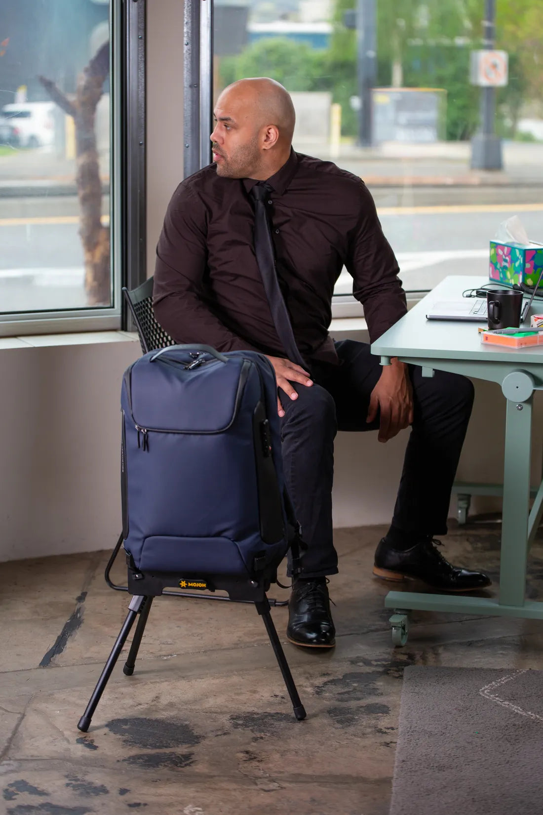 A commuter at an office desk with his backpack held upright on the Ryzer Go beside him