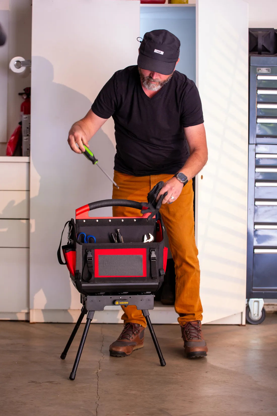 A tradesman standing over his tool bag held upright on the Ryzer Go in a garage workshop